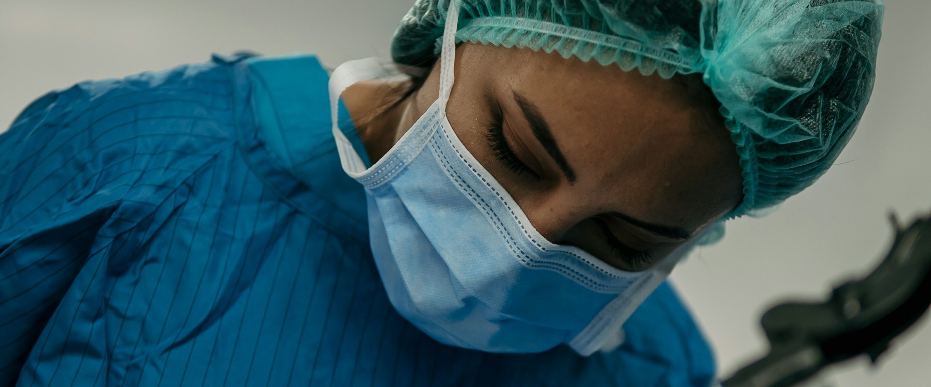 Close-up of a surgeon in mask and surgical cap looking down in concentration