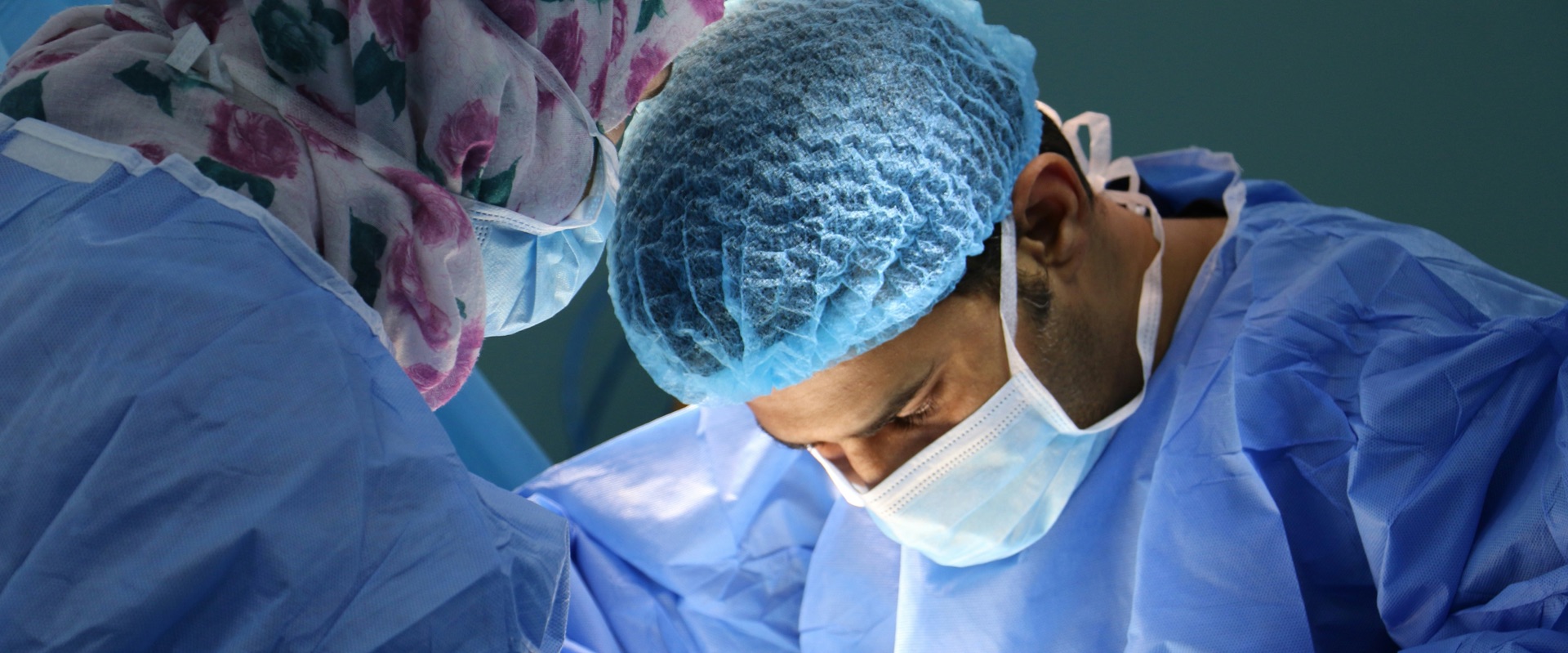 Two surgeons in blue caps and masks focused on a procedure in the operating room
